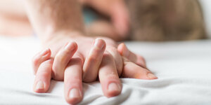 Hände eines Mannes und einer Frau verschränkt auf einem weißen Bettlaken