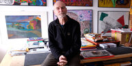 Fotograf Peter Leske sitzt in seinem Atelier vor Kunstwerken an der Wand