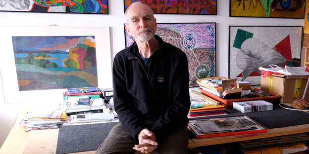 Fotograf Peter Leske sitzt in seinem Atelier vor Kunstwerken an der Wand