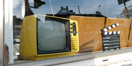 Ein sehr altes, dottergelbes Modell eines Fernsehers steht in einem Schaufenster