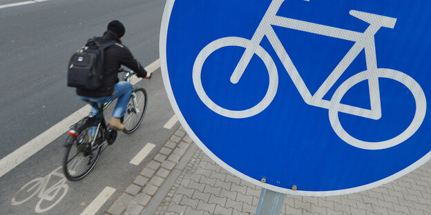 Ein Fahrradfahrer fährt auf einem Radweg an einem Verkehrsschild vorbei
