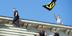 Ein Identitärer steht auf einem Dach und schwenkt die IB-Fahne