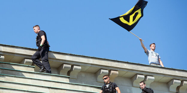 Ein Mann schwenkt eine Fahne. Er steht auf einem Sockel. Polizisten sind in der Nähe