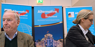 Alexander Gauland und Alice Weidel sitzen vor drei Bannern der AfD. Gauland sitzt links und schaut nach links aus dem Bild heraus, Weidel sitzt rechts und schaut rechts unten aus dem Bild heraus.