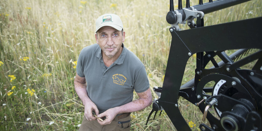 Frank Hartmann steht in seinem Feld, neben ihm ein Mähdrescher