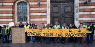 Menschen mit gelben Westen demonstrieren und tragen ein Transparent gegen Rassismus