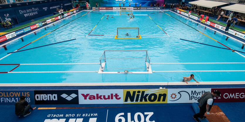 Zwei Männer verlegen bei der Schwimm WM einen Teppich mit dem Logo der WM am Rande des Trainings einer Damen-Wasserball-Mannschaft