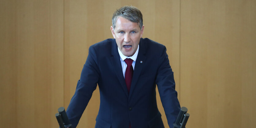 Björn Hocke steht in einem dunkelblauen Anzug an einem Pult und redet.