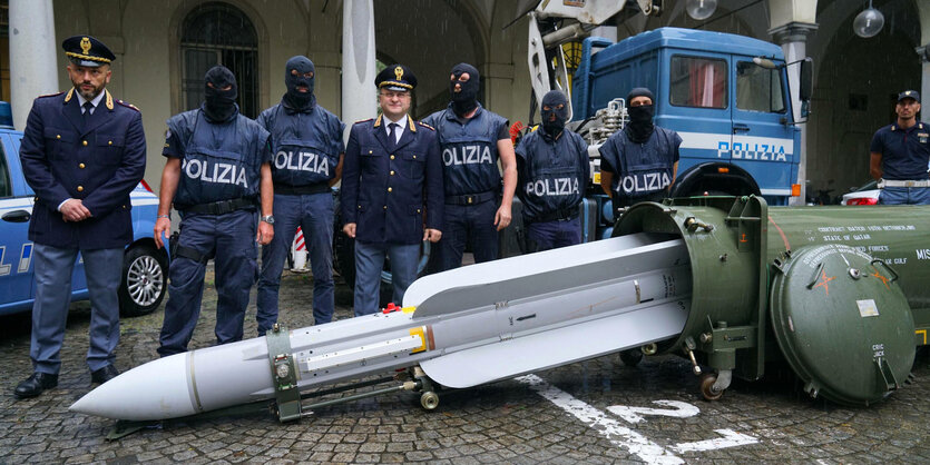 Polizisten stehen hinter einer Rakete, die in einem Flughafenhangar beschlagnahmt wurde