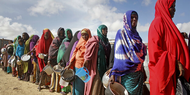 Frauen stehen mit Behältern in einer Schlange um Essen zu erhalten