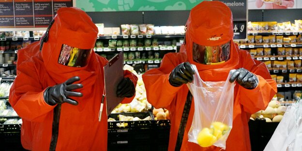 Zwei Personen in orangenen Schutzanzügen in einem Supermarkt