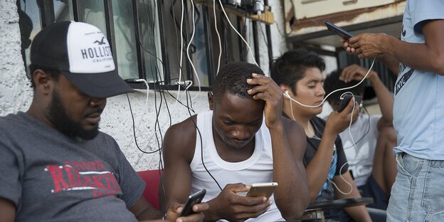 Geflüchtete aus Kamerun warten vor der US-Asylbehörde und laden ihre Handys