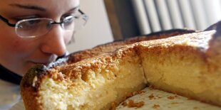 Eine Frau riecht an einem aufgeschnittenen Käsekuchen