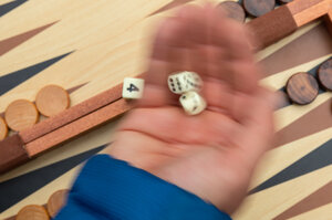 Würfel in einer Hand vor einem Backgammon-Spielbrett Würfel in einer Hand vor einem Backgammon-Spielbrett