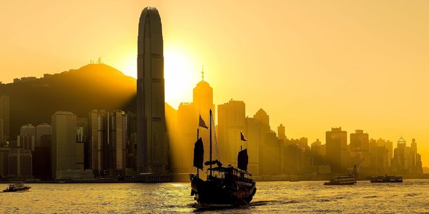 Skyline von Hongkong in der Abendsonne, auf dem Wasser ein Boot