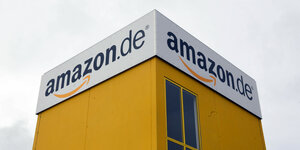Man sieht ein amazon.de-Logo auf zwei Seiten eines Logistikgebäudes.