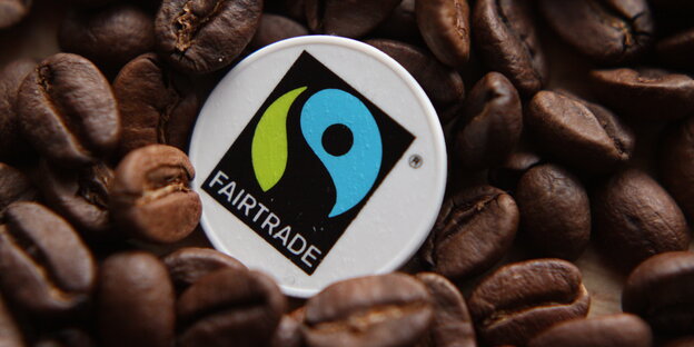 Kaffeebohnen, darin ein Schild, auf dem Fairtrade steht, auf Deutsch: Fairer Handel