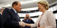 Silvio Berlusconi schüttelt Ursula von der Leyen die Hand, beide lächeln.
