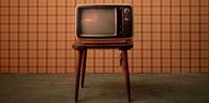 Ein Fernseher aus den 70er-Jahren steht vor einer braun tapezierten Wand.