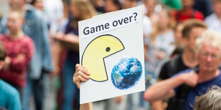 Auf einer Fridays-for-Future-Demonstration hält jemand ein Schild in die Luft. Darauf ist ein Packman, der die Erde frisst und ein Schriftzug: "Game over?"