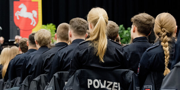 Eine Gruppe von Polizeianwärtern von hinten vor dem niedersächsischen Wappen