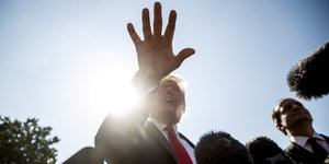 Ein Mann, Donald Trump, hält die Hand ins Bild, an der Seite sind Mikrofone. Ein zweiter Mann steht neben ihm