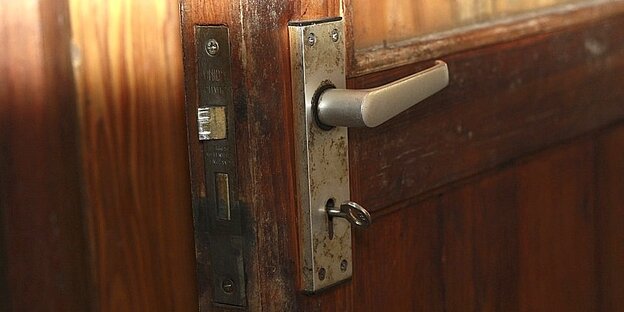 In einem Türschloss an einer hölzernen Tür steckt ein Schlüssel.