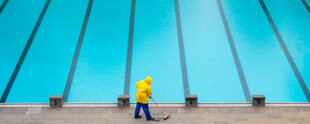 Mitarbeiter mit gelber Jacke fegt neben leerem Schwimmbecken