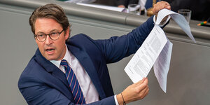 Mann in einem Anzug steht am Rednerpult im Bundestag und hält Papiere in die Höhe.