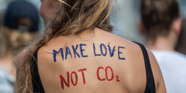 Auf dem Rücken einer jungen Frau steht mit blauer und roter Farbe: Make Love Not CO2