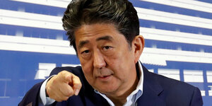 Shinzo Abe blickt konzentriert ind ie Kamer aund deutet mit dem Zeigefinger in deren Richtung