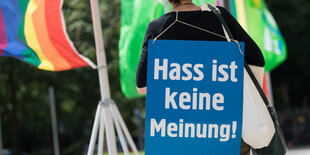 Eine Frau steht mit dem Rücken zur Kamera. Auf ihrem Rücken hängt ein großes Plakat mit der Aufschrift "Hass ist keine Meinung".