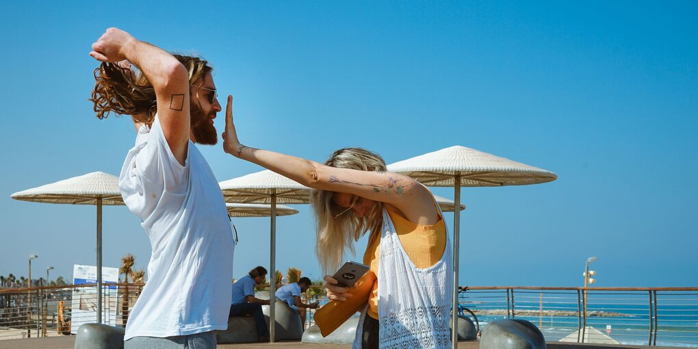 ein Pärchen steht am Strand von tel Aviv, sie hält ihm den Mund zu