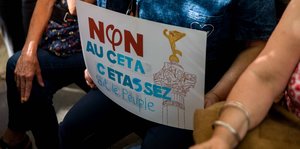 Eine Demonstrantin hält ein Protest-Schild gegen Ceta in ihrem Schoß