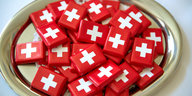 Man sieht kleine Schokotafeln, die in Papier mit der Schweizer Flagge eingepackt sind