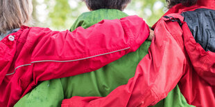 Drei Frauen tragen Regenjacken in roter und grüner Farbe.