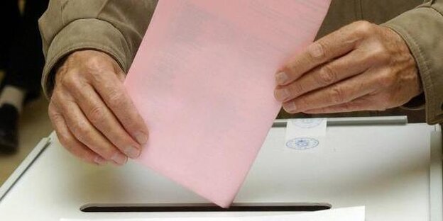 Ein rosafarbener Wahlzettel wird in eine Wahlurne gesteckt