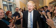 Boris Johnson läuft lächelnd durch einen Gang, rechts und links applaudieren Menschen