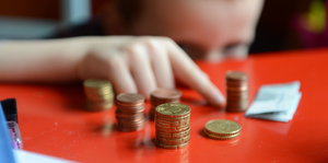 Taschengeld für Heimkinder: Ein Kind stapelt und Zählt Münzen und einen Fünf-Euro-Schein