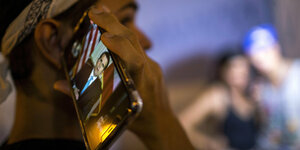 Ein Mann hält sich ein Handy ans Ohr. Auf dem Display ist ein Video zu des puertoricanischen Präsidenten zu sehen