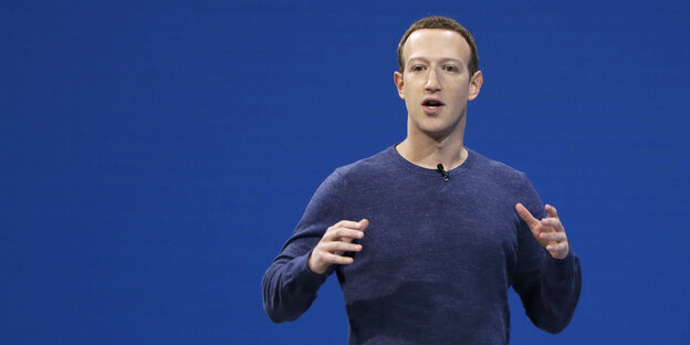 Zuckerberg gestikuliert vor einem blauen Hintergrund