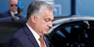 Orban im Profil, er schaut vor sich auf den Boden, dahinter ein Auto