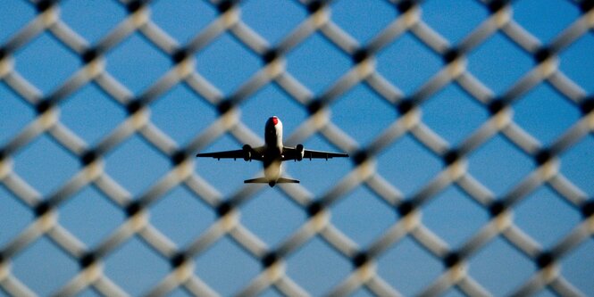 Ein Flugzeug in der Luft, davor ein Maschendrahtzaun