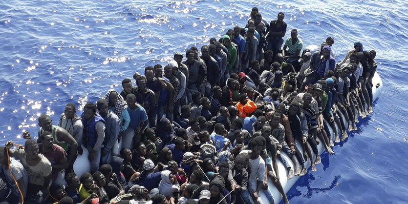 Viele Menschen sitzen eng nebeneinander auf einem Gummiboot im Meer