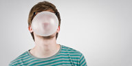 Ein Mann macht eine Kaugummiblase, die sein Gesicht verdeckt