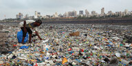 Mann sammelt Müll am Ufer. Im Hintergrund Hochhäuser