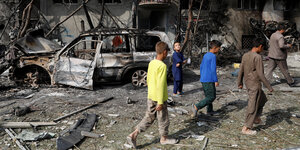 Kinder laufen an einem ausgebrannten Auto und Trümmern vorbei
