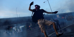 Ein vermummter Demonstrant im Rauch hebt eine Hand