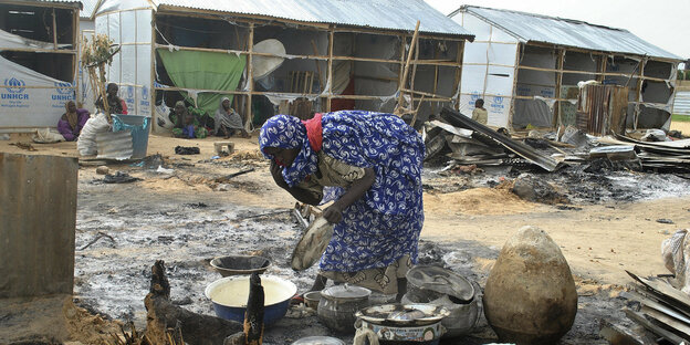Eine Frau steht auf einer nigerianischen Straße in Trümmern und kocht