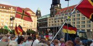 Eine Menschenmenge, über der ein paar Deutschlandflaggen und rote Flaggen mit rotem Kreuz wehen